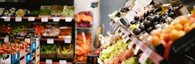Fresh produce display at grocery store with colorful fruits and vegetables arranged on tiered shelves, including tomatoes and apples