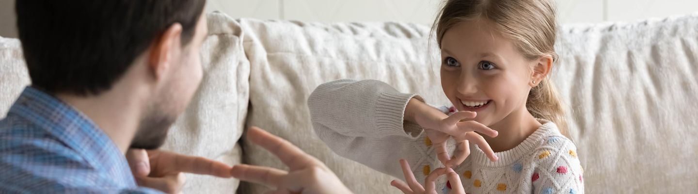 Therapist training smiling child with hearing disability using hands and fingers for communication.