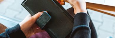 Hands holding a black leather wallet with credit cards visible inside, photographed in natural lighting