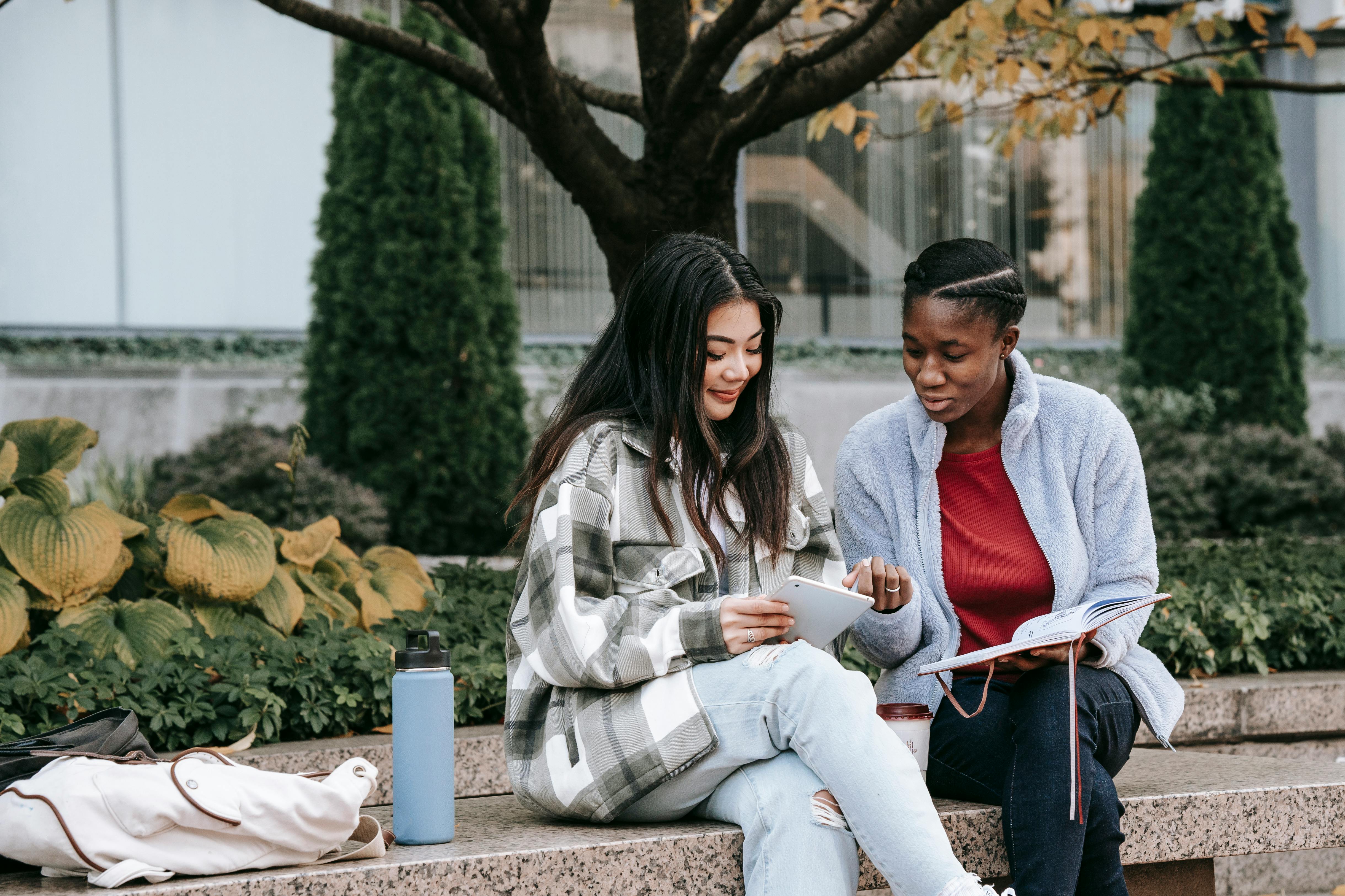 2 girls discussing something with a book and a tablet