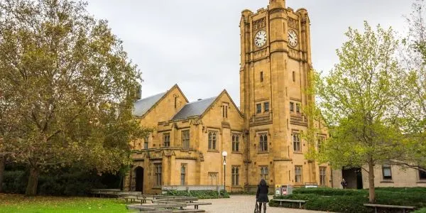 Historic sandstone Gothic Revival university building with tall clock tower and arched windows surrounded by autumn trees