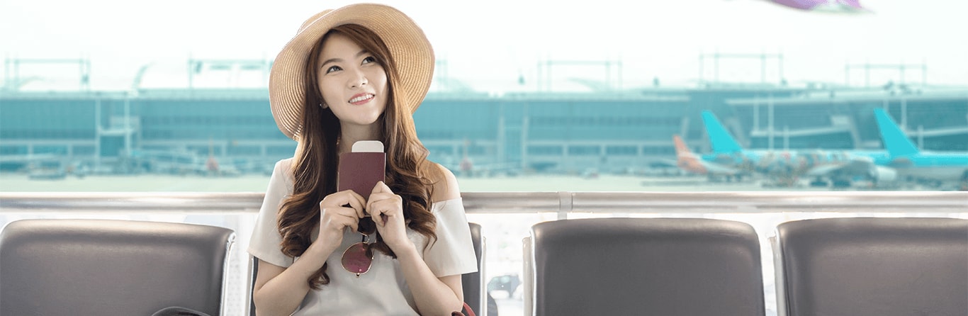 Woman wearing straw hat holding passport sitting in airport smiling