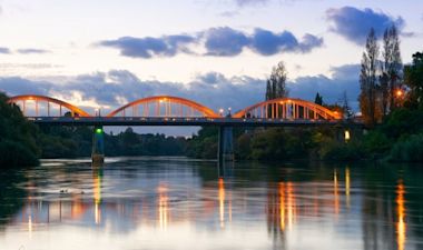 A well lit bridge on an evening across a river with its reflection over the water