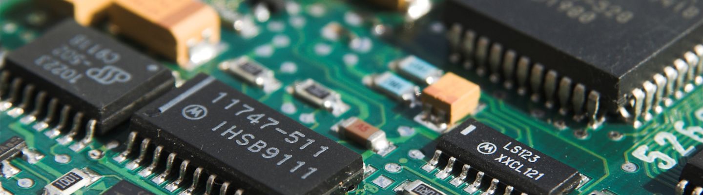 Close-up view of electronic circuit board with integrated chips, resistors, and components on green PCB surface