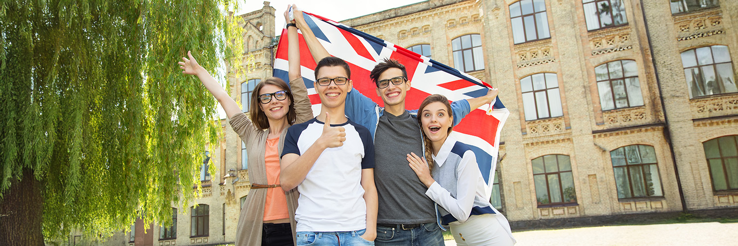 Group of students holding a flag of Great Britain on the university campus background. Friends in United Kingdom.