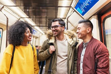 Three friends smiling and looking at each other on a train. The friend in the middle is wearing a jacket.