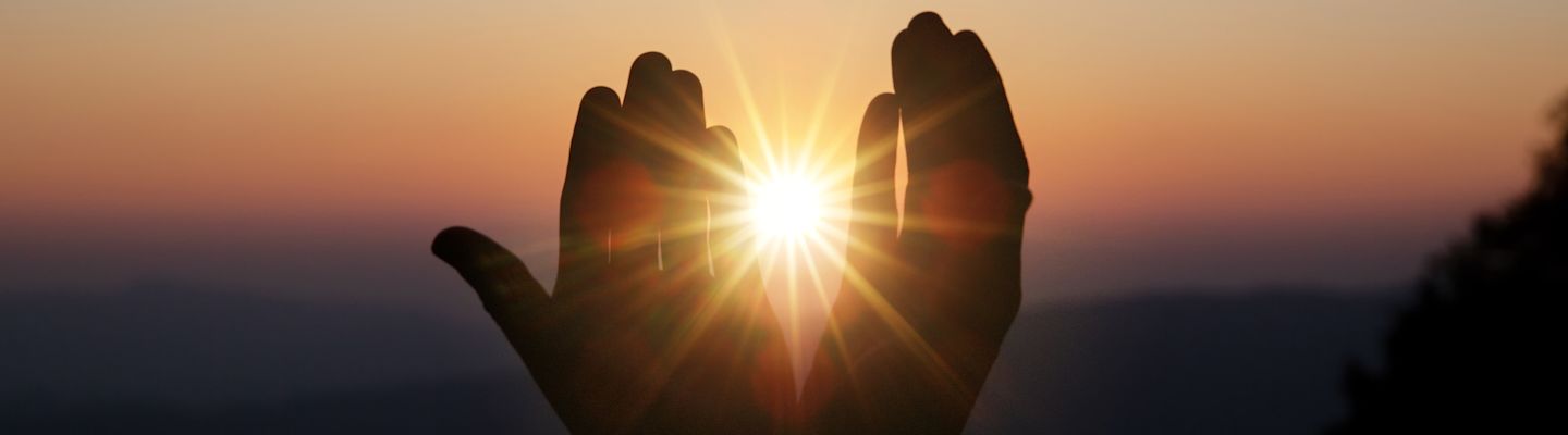 Hands joined during a religious worship with sunshine in the background.