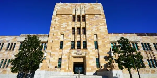 Art Deco style sandstone building with vertical columns and symmetrical design against bright blue sky, flanked by trees