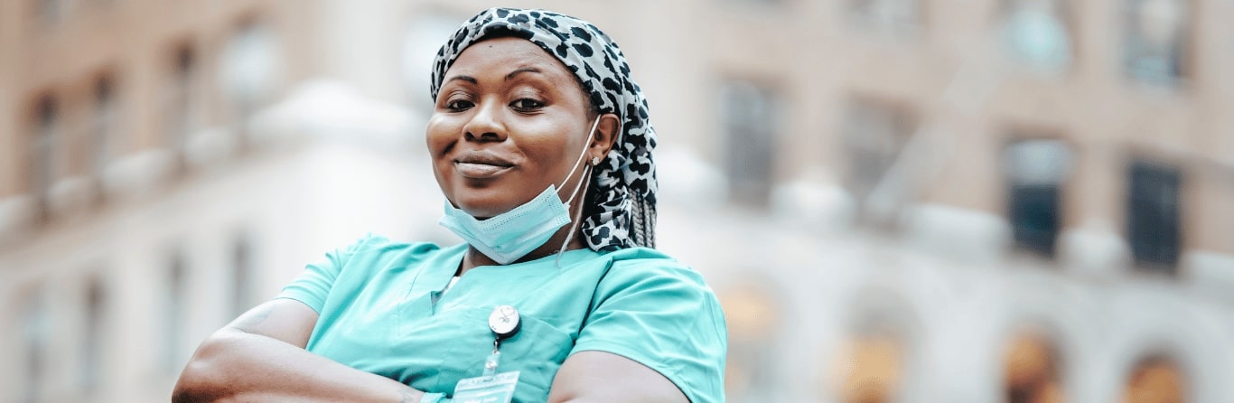 A lady nurse is standing infront of an institution in her nursing uniform