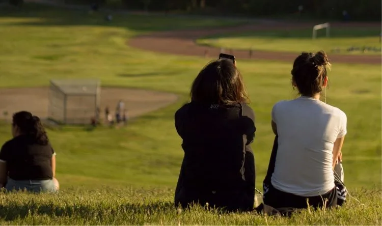 Two students looking sitting on grass and watching a playground