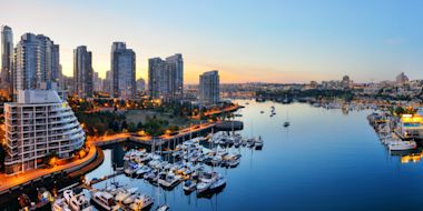  Aerial view of Vancouver marina at dusk with illuminated waterfront, luxury boats docked at curved harbor, and high-rise buildings in background