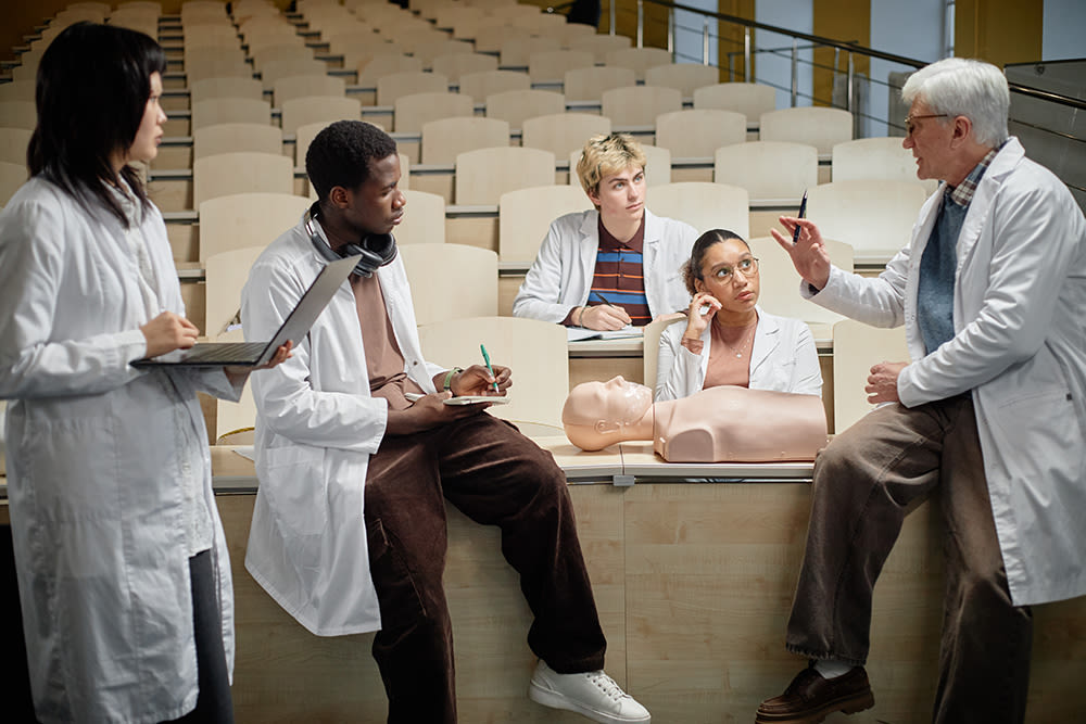 Professor explaining CPR technique to med students practicing with torso dummy during lecture in university classroom