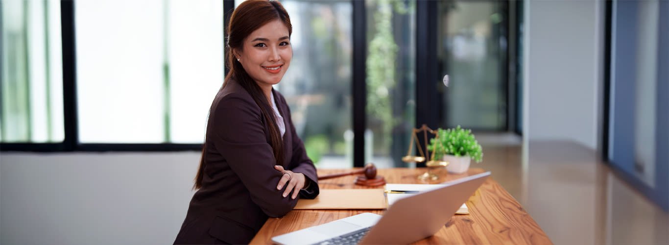 Counsellor sits at a desk, looking at the camera and smiling