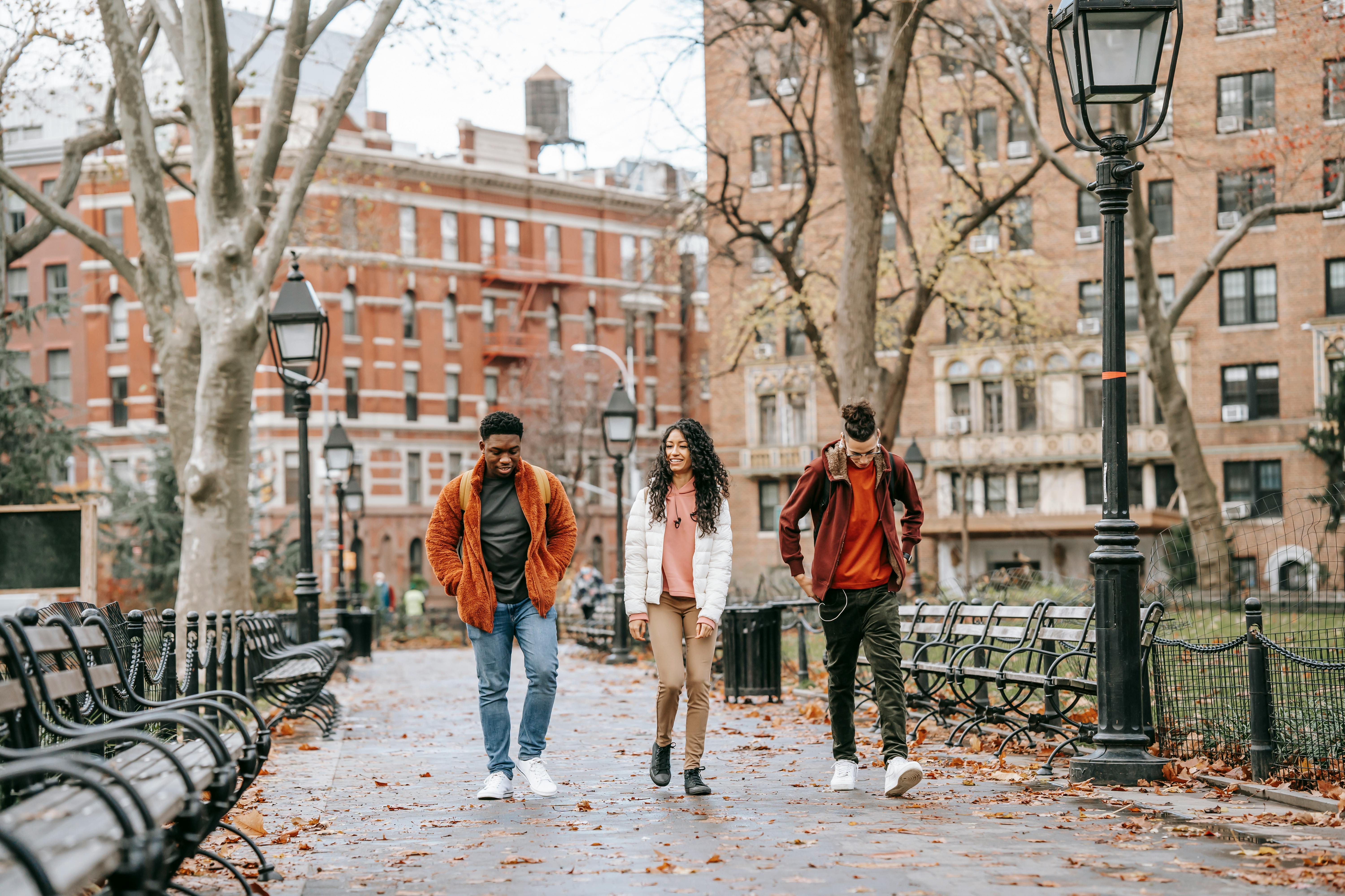 Three students walking in front of a campus in Autumn clothing