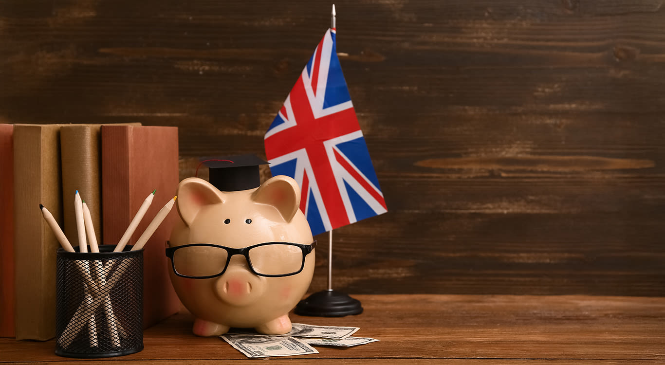 Piggy bank with money, books and UK flag on wooden table.