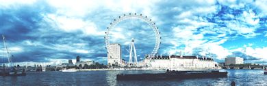 A panoramic view of the London Eye on the River Thames under a partly cloudy sky. The iconic Ferris wheel stands tall amidst nearby buildings. Boats are visible on the water, enhancing the vibrant cityscape.
