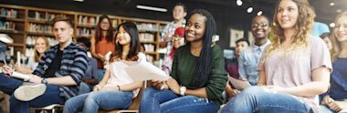 Diverse group of students sitting together in a library or study space, smiling and holding papers during a class or study session
