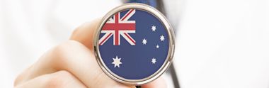 A hand holding a stethoscope with the Australian flag design on the diaphragm, against a light background.