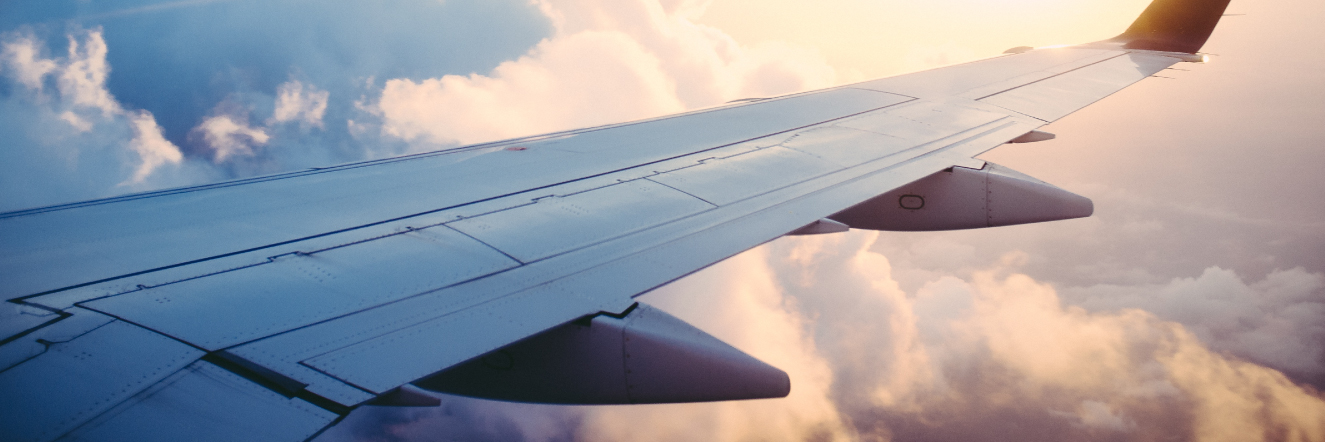 View from an airplane window showing a wing against a backdrop of fluffy clouds and a glowing sunset sky. The scene conveys a sense of calmness and serenity at high altitude.
