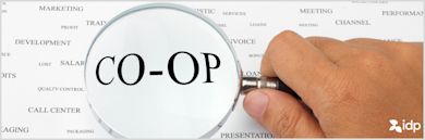 A hand holds a magnifying glass over the word CO-OP on a sheet filled with other business-related words such as MARKETING, CHANNEL, and CALL CENTER.