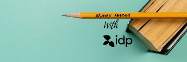 A yellow pencil with Study Abroad written on it rests on an open book. The words with idp and the idp logo are beside the pencil on a light blue background.