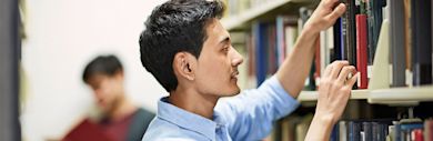 An international student taking a book from a shelf in a library