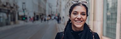 An international student wearing a scarf and sunglasses smiling