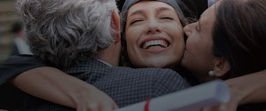 An international student wearing a graduation robe and holding a degree hugs her parents.