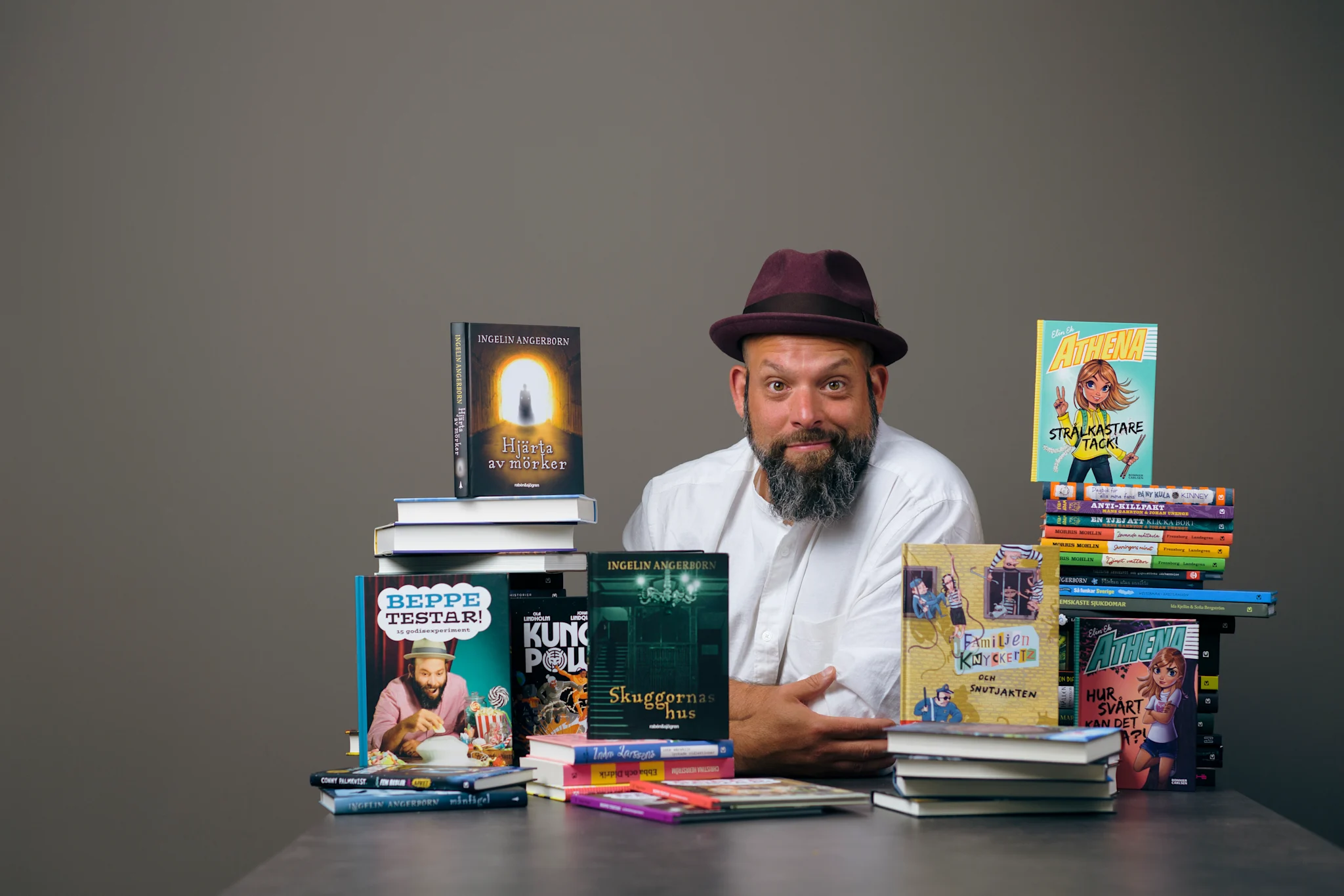 Porträtt av Beppe Singer med böcker i olika genrer runt omkring.