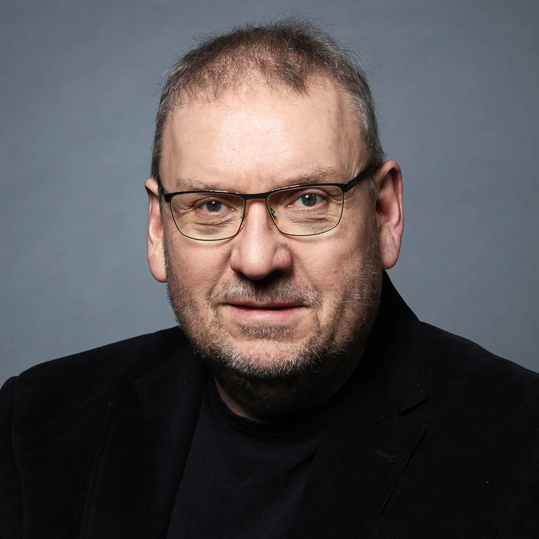 Författarporträtt av Anders Nilsson, sittande i en svart kavaj mot en grå bakgrund.