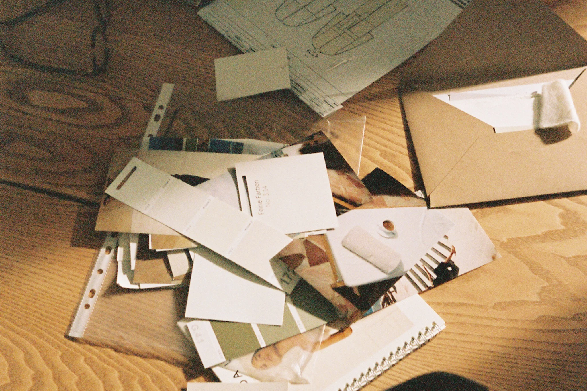 Kasa erilaisia papereita, värinäytteitä ja valokuvia puupöydällä.