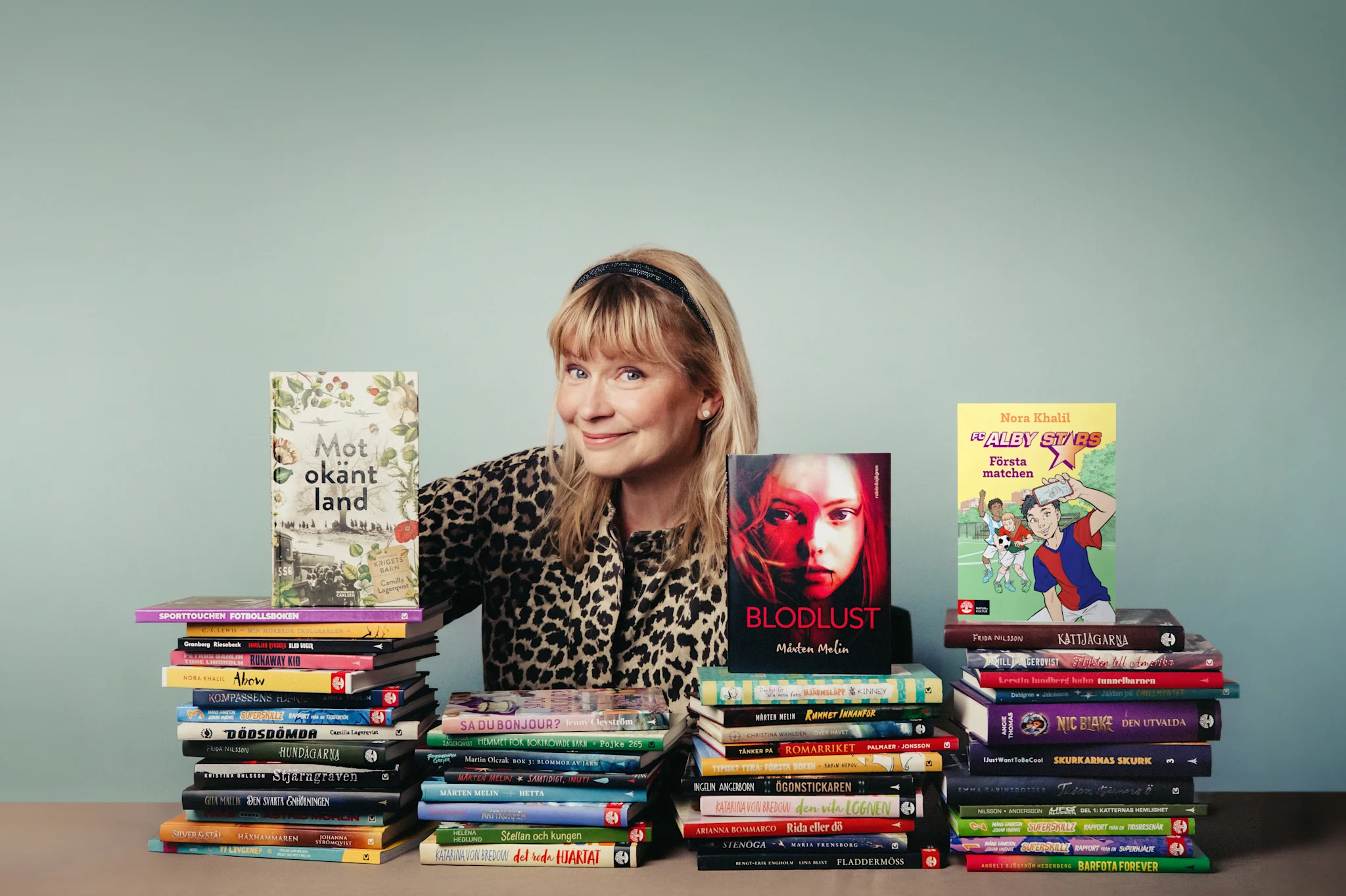 En person står mellan staplar av böcker, med titlar som 'Mot okänt land' och 'Blodlust'.