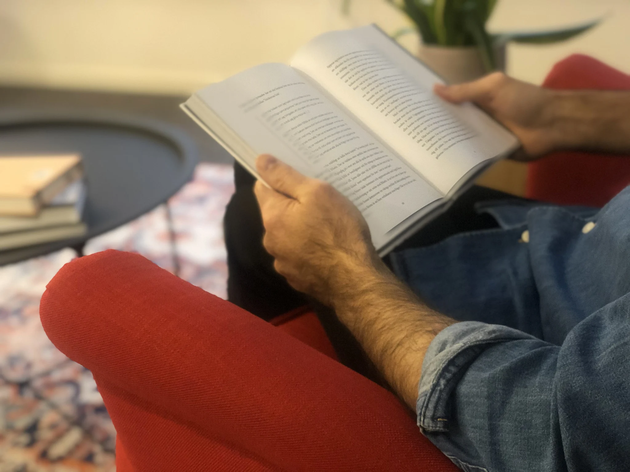 Mann leser en åpen bok mens han sitter i en rød lenestol.
