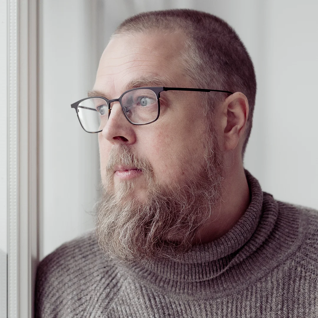 Kirjailijan muotokuva Tuomas Kyröstä, keskittyen hänen hiuksiinsa ja vaatteisiinsa.