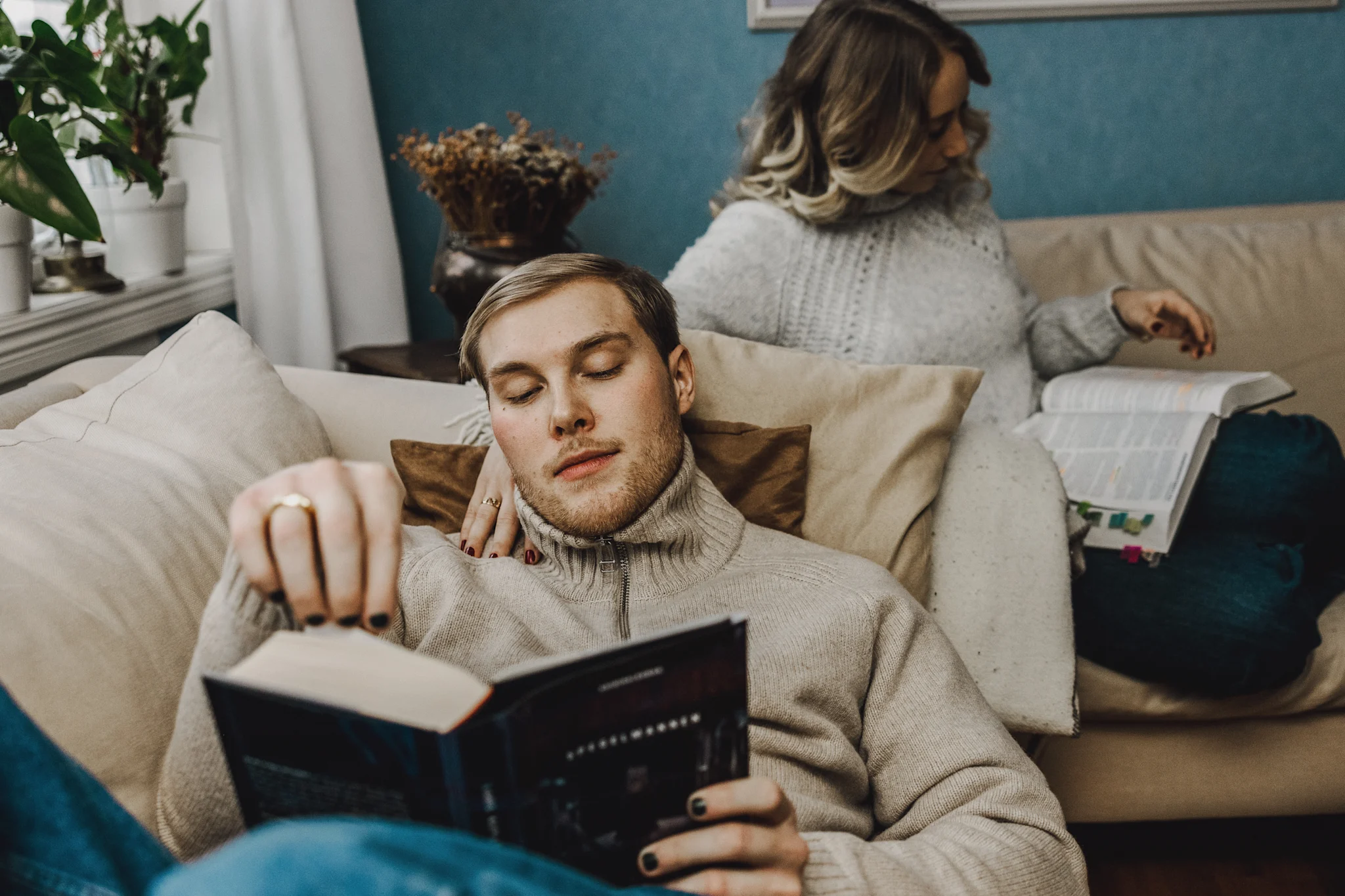 To studenter sitter i en sofa og leser bøker i et koselig miljø.