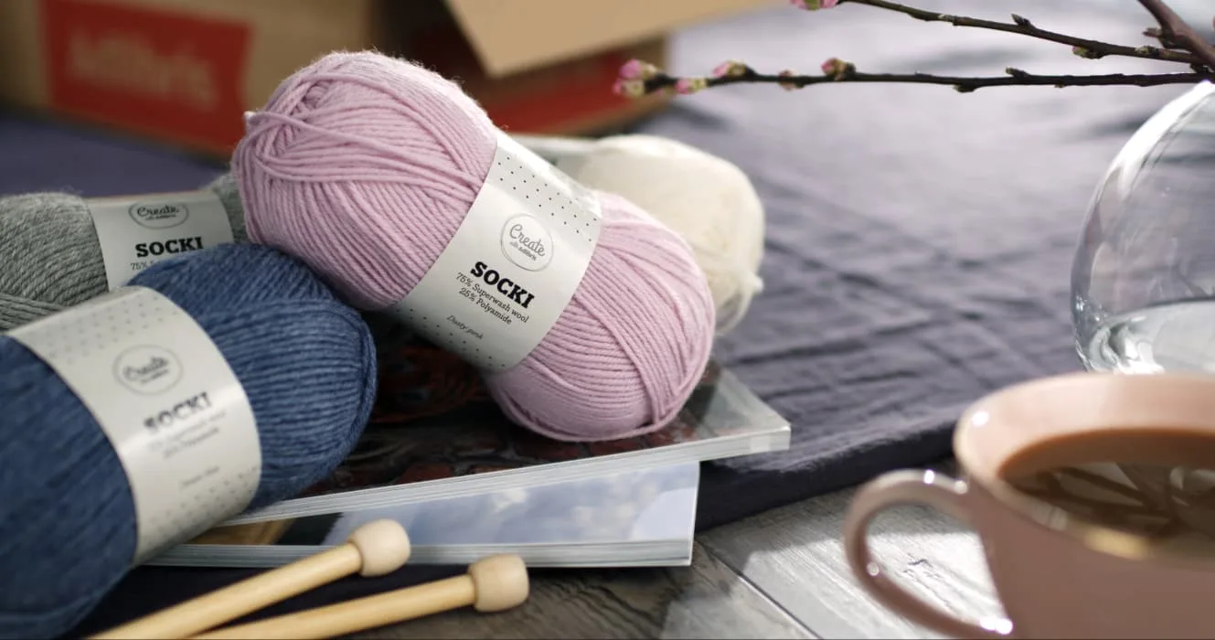 Kuva erilaisista lankakeristä etiketteineen, kahvikupista ja maljakosta pöydällä.