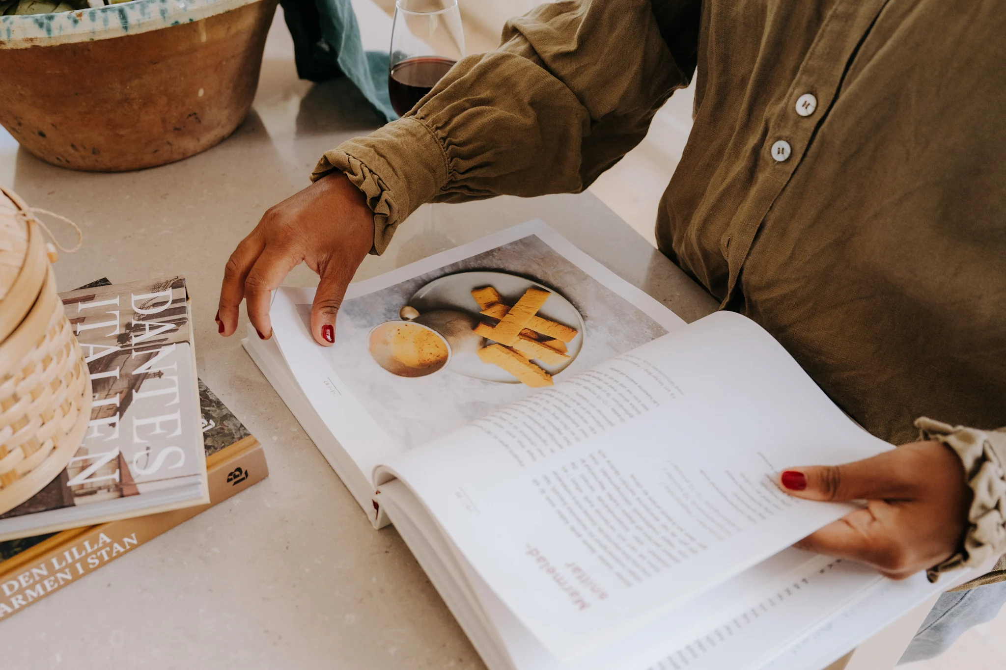 En hand bläddrar i en kokbok som visar en tallrik med mat och en kopp med dryck.