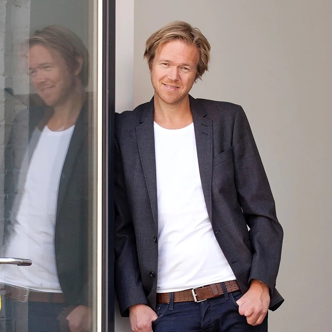 Bilde av forfatter Ole Andre Sivertsen, kledd i dressjakke og t-skjorte, lent mot en vegg.