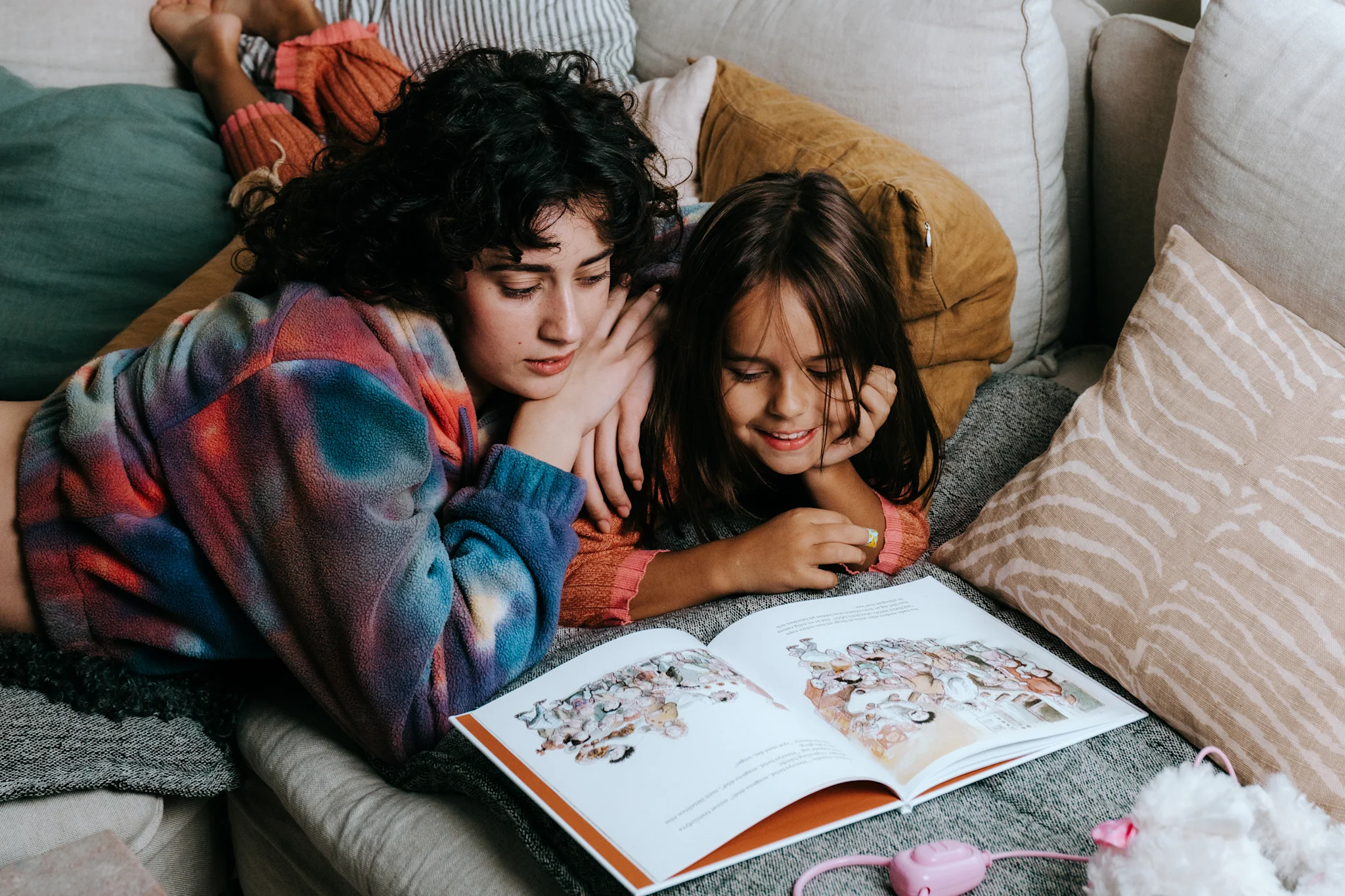 To barn som leser en bok sammen i en koselig sofa.