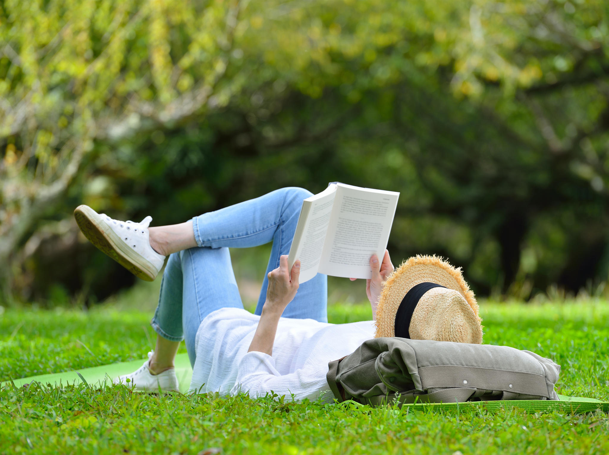 Person i stråhatt läser en bok utomhus i grönt gräs. 