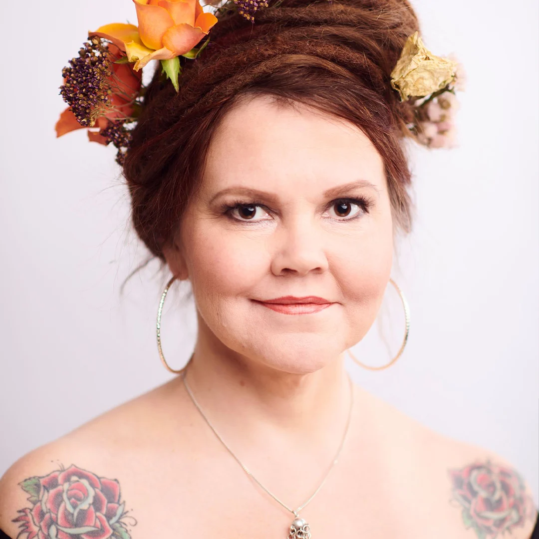 Kirjailijan muotokuva Katja Kettusta, jossa kukkia hiuksissa ja tatuointeja olkapäillä.