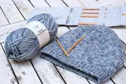Bilde av en grå lue med perlestrikk og et garnnøste av Socki Stonewash.
