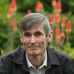 Författaren Andrew Miller sitter i en blomstrande trädgård omgiven av färgglada blommor och grönska.