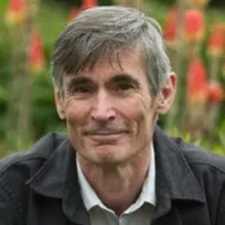 Författaren Andrew Miller sitter i en blomstrande trädgård omgiven av färgglada blommor och grönska.