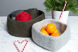 To filtede kurver med garn og appelsiner, en grå og en grønn, på et marmorbord.