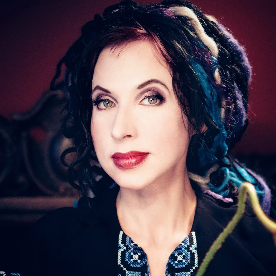 Författarporträtt av Sofi Oksanen med färgglada lockar i en mörk miljö.