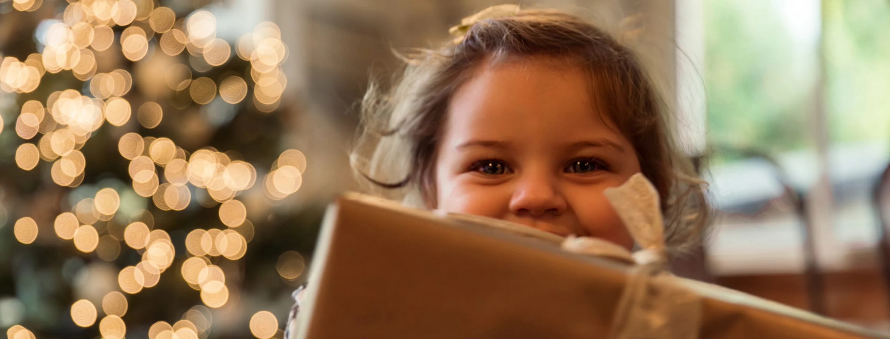 A smiling little girl holding a Christmas present in front of her face