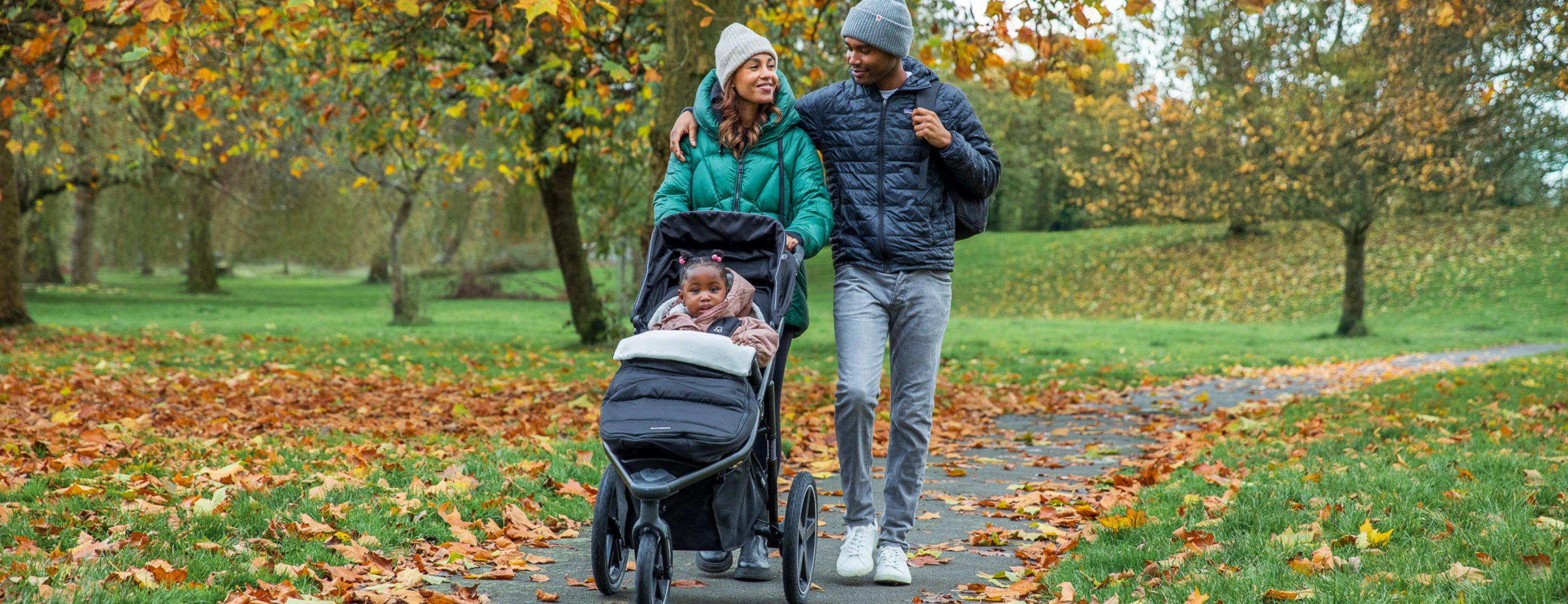 A family strolling in a park with a running pushchair