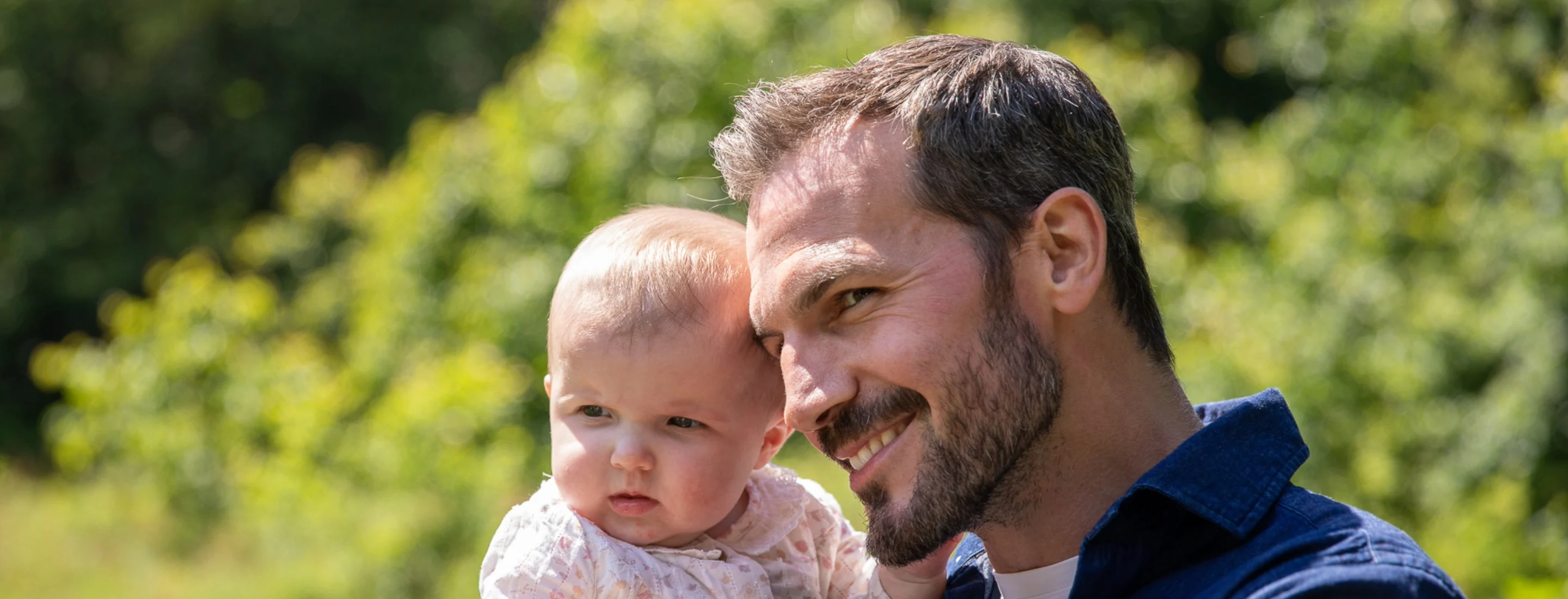 A man holding a baby and pointing on a sunny day