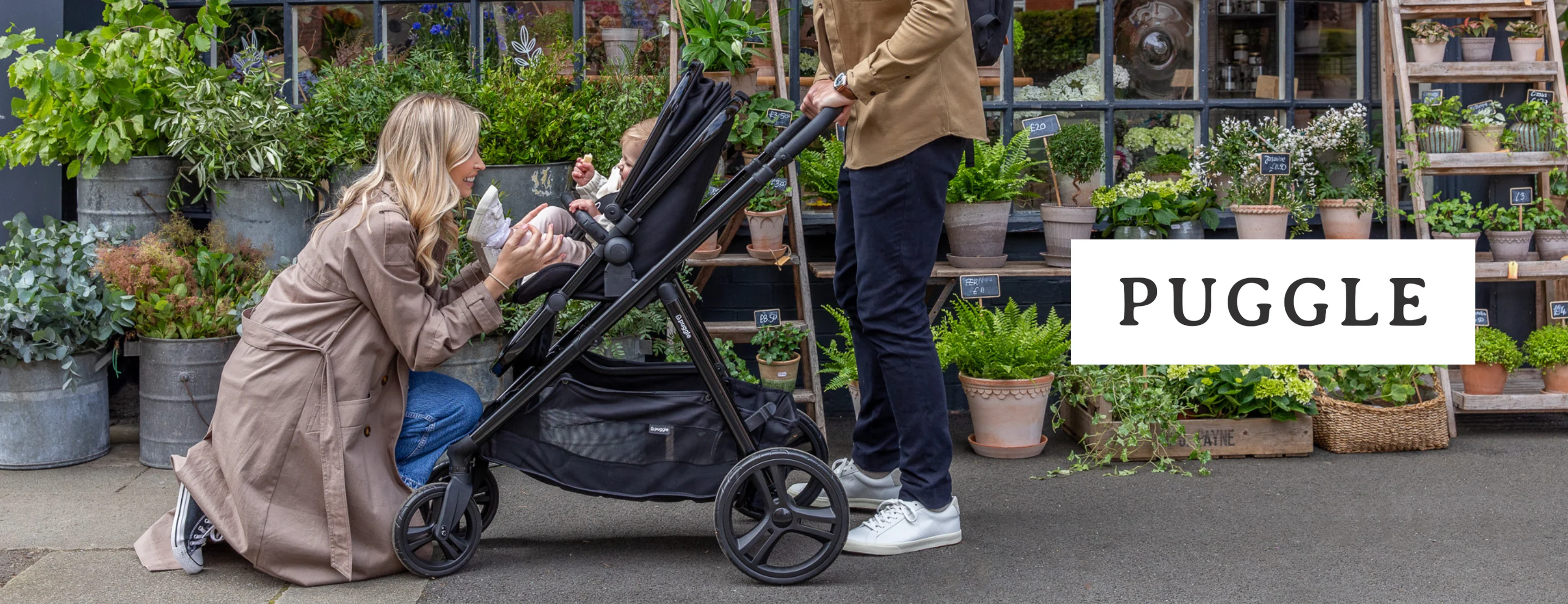 a mum kneeling down to play with her daughter sitting in a black Puggle pushchair